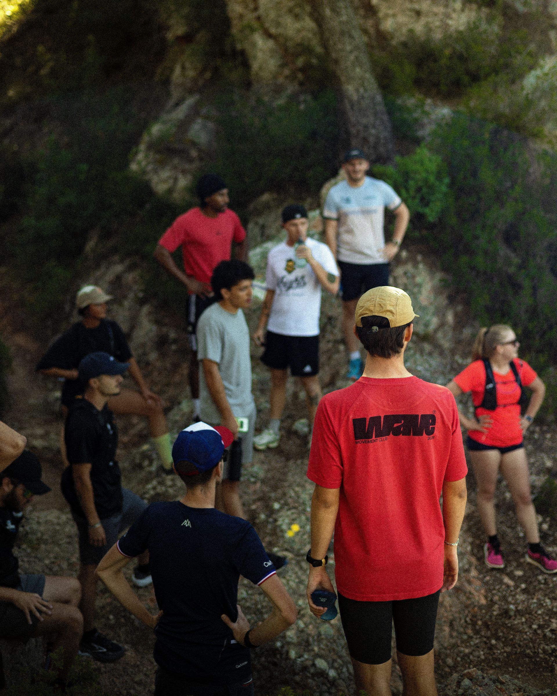 Au briefing d’une sortie en forêt, un coureur de dos porte le T-shirt rouge WAVE 2026, floqué WAVE Movement Club 2026.
